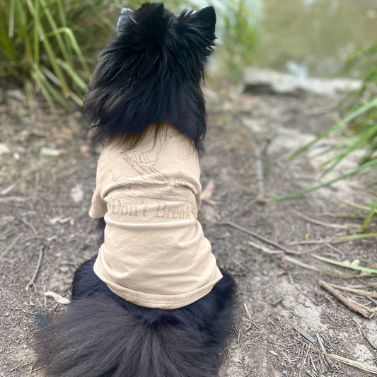 Kuma the black Pomeranian, sits with his back fully turned, showcasing the ‘Bend Don’t Break’ tee in sand with a gold lustre print. This subtle tone-on-tone design reflects understated elegance, complementing the natural landscape. Made with sustainable 190GSM Good Earth Cotton® for comfort and style.