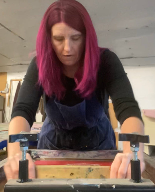 Mel in the Fur‑You studio, wearing her signature magenta hair and holding a squeegee, front on and focused, about to pull a screen print