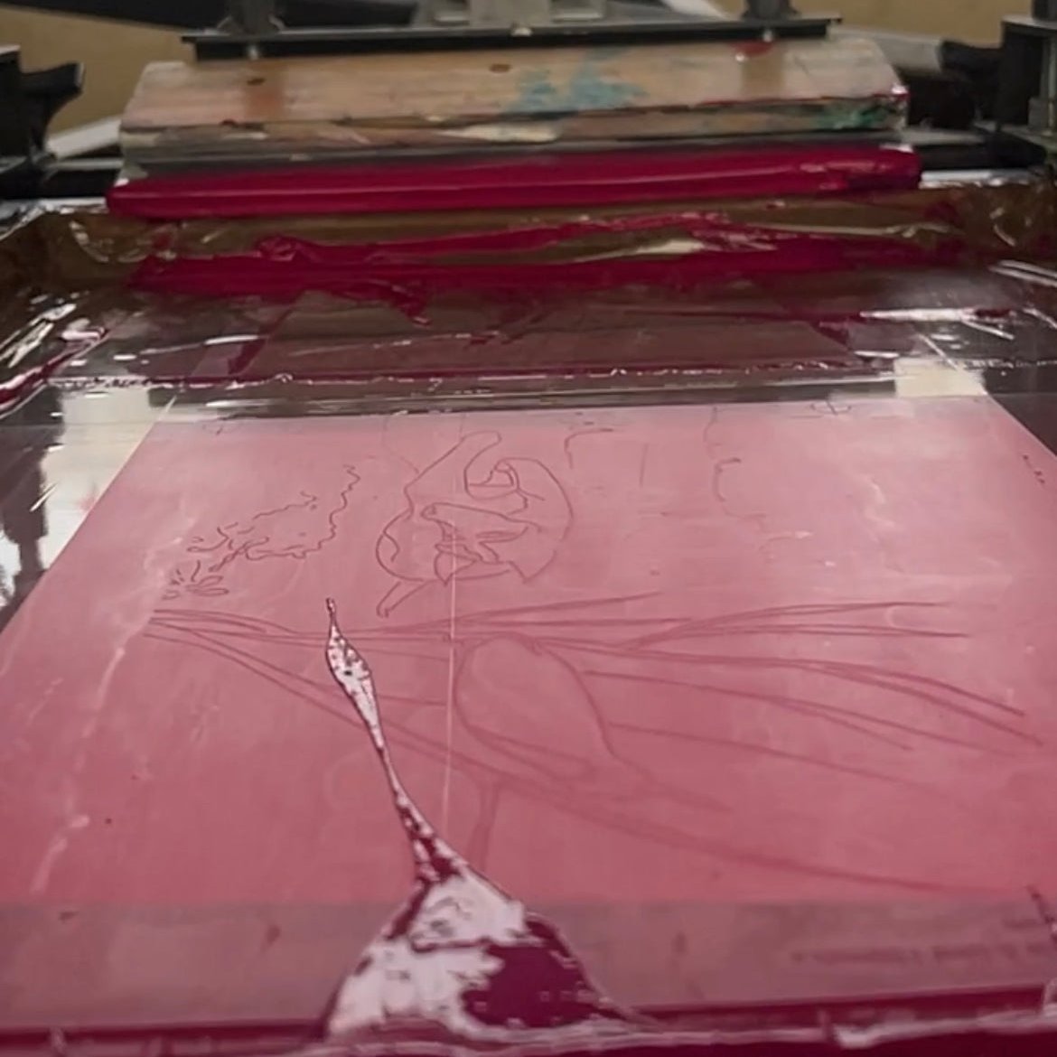 screen print screen showing stencil of Charlke and the bird with pink ink just printed, ink both at the top and bottom of the inside screen and a squeegee resting in the top distance of screen