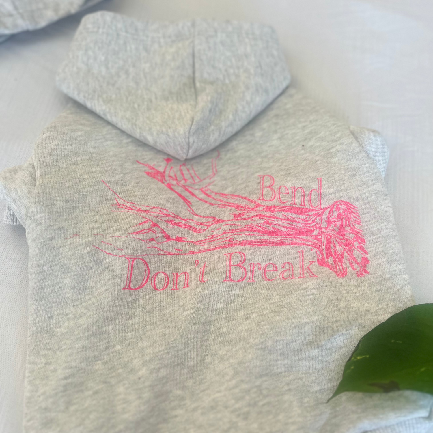 Flat lay of Fur-You’s ‘Bend Don’t Break’ hoodie in glow pink print on grey marle, now neatly folded back hood to highlight the artistic tree design. A sustainable and stylish choice for pets
