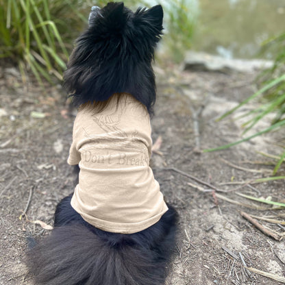 Kuma the black Pomeranian, sits with his back fully turned, showcasing the ‘Bend Don’t Break’ tee in sand with a gold lustre print. This subtle tone-on-tone design reflects understated elegance, complementing the natural landscape. Made with sustainable 190GSM Good Earth Cotton® for comfort and style.